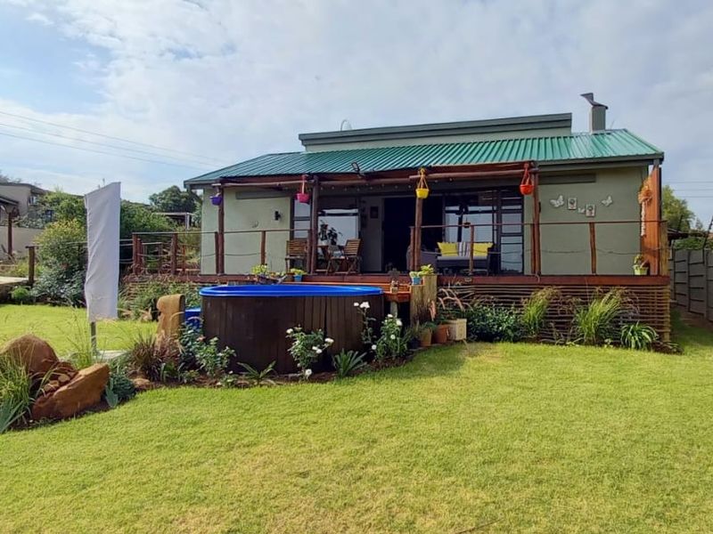 Rear view of the property featuring a green metal roof, a wooden deck, and a small plunge pool set within a landscaped garden.