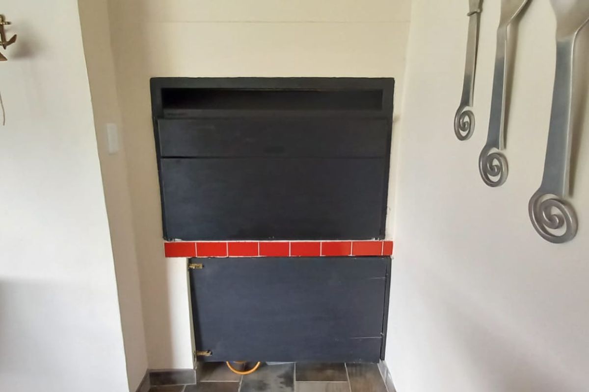 A built-in indoor braai unit featuring a black finish and a red tiled hearth, situated within a neutral-toned living space.
