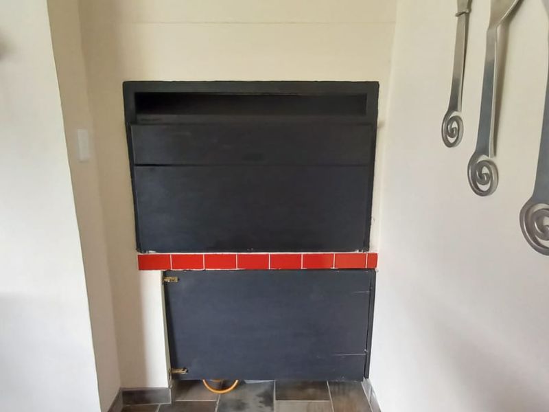 A built-in indoor braai unit featuring a black finish and a red tiled hearth, situated within a neutral-toned living space.