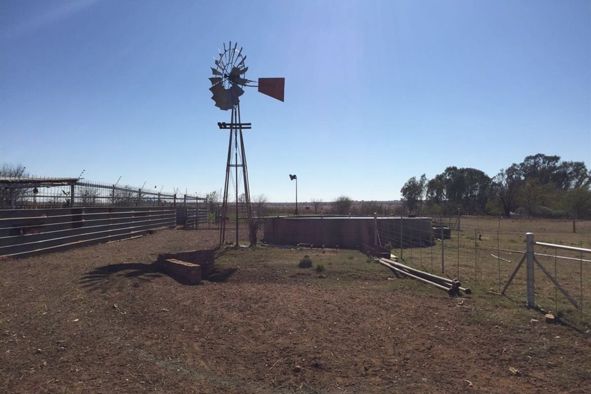 Outdoor farm area featuring a traditional windmill, water reservoir, and livestock fencing on open land.