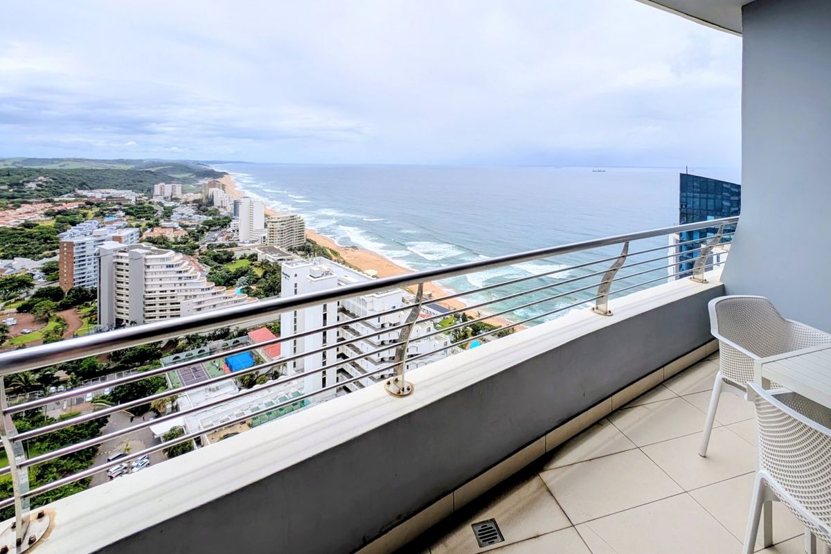 A spacious balcony featuring a stainless steel balustrade and tiled flooring, offering expansive coastal and urban views.