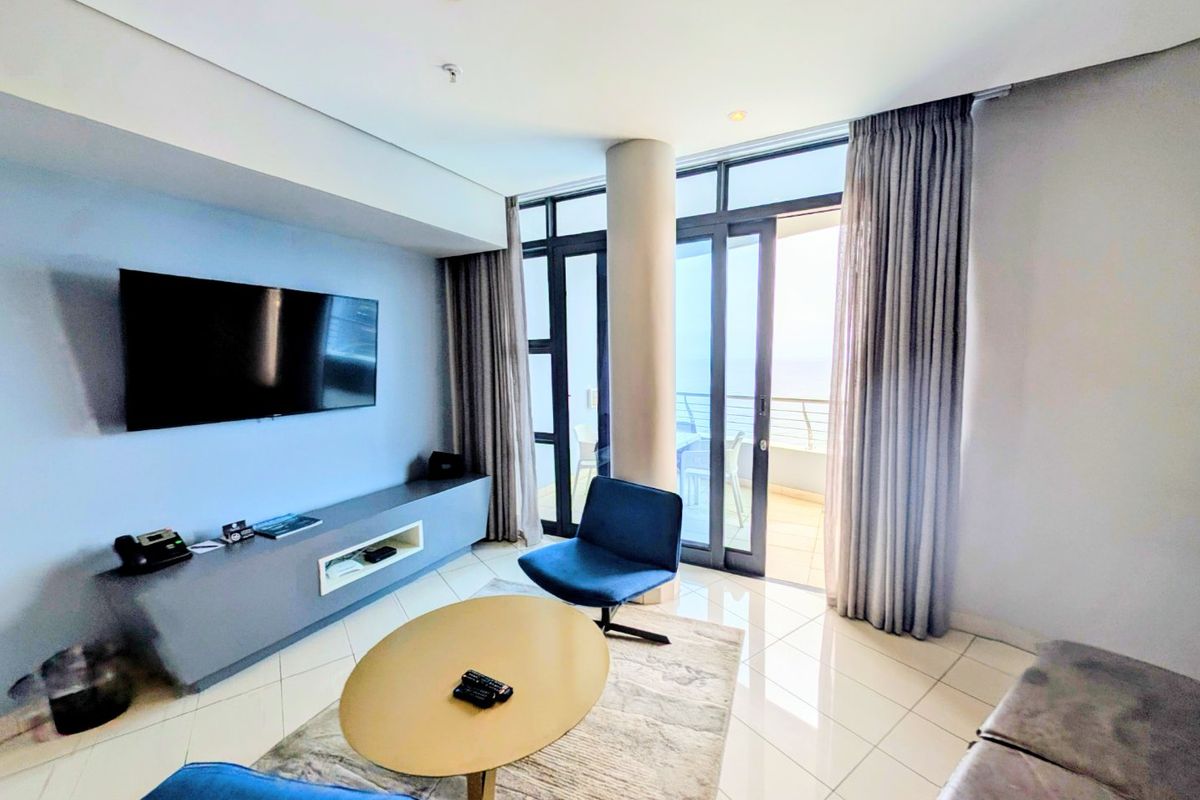 A bright living room featuring tiled floors, a built-in media console, and large sliding glass doors providing access to a balcony with natural light.