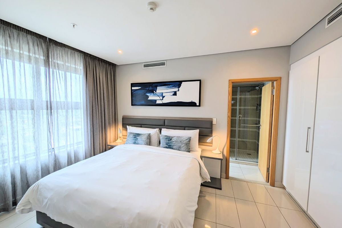 A modern bedroom featuring tiled floors, built-in wardrobes, and an en-suite bathroom with a glass-enclosed shower.