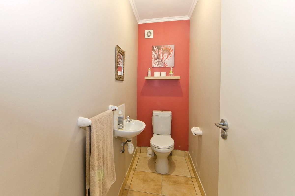 A compact guest bathroom featuring a wall-mounted basin, a standard toilet, tiled flooring, and an extractor fan.