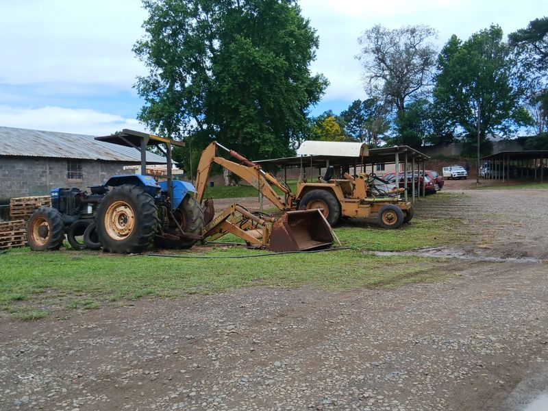 A large gravel farm yard featuring a metal-roofed storage shed and covered parking structures for machinery and vehicles.