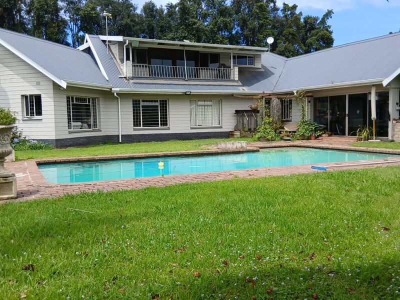 Rear view of the farmhouse featuring a swimming pool, brick-edged patio, and a second-story balcony overlooking the garden.