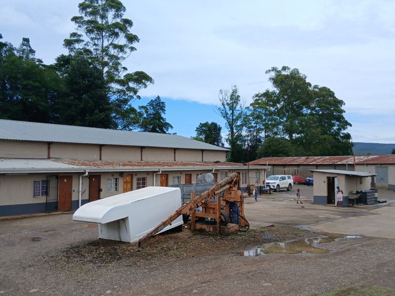 Rear view of farm outbuildings featuring corrugated metal roofing and a large concrete yard area, showing signs of age and wear.