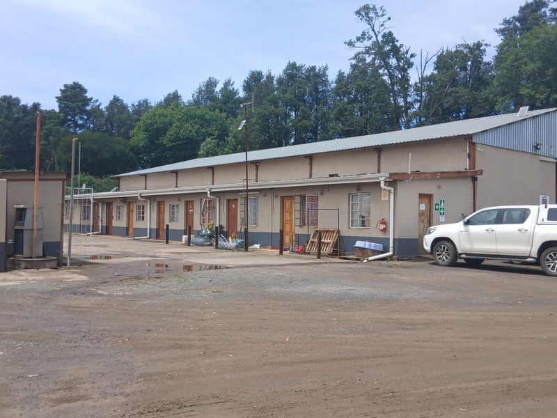 Exterior view of a long industrial-style farm building featuring multiple access doors, metal roofing, and a large unpaved yard area.