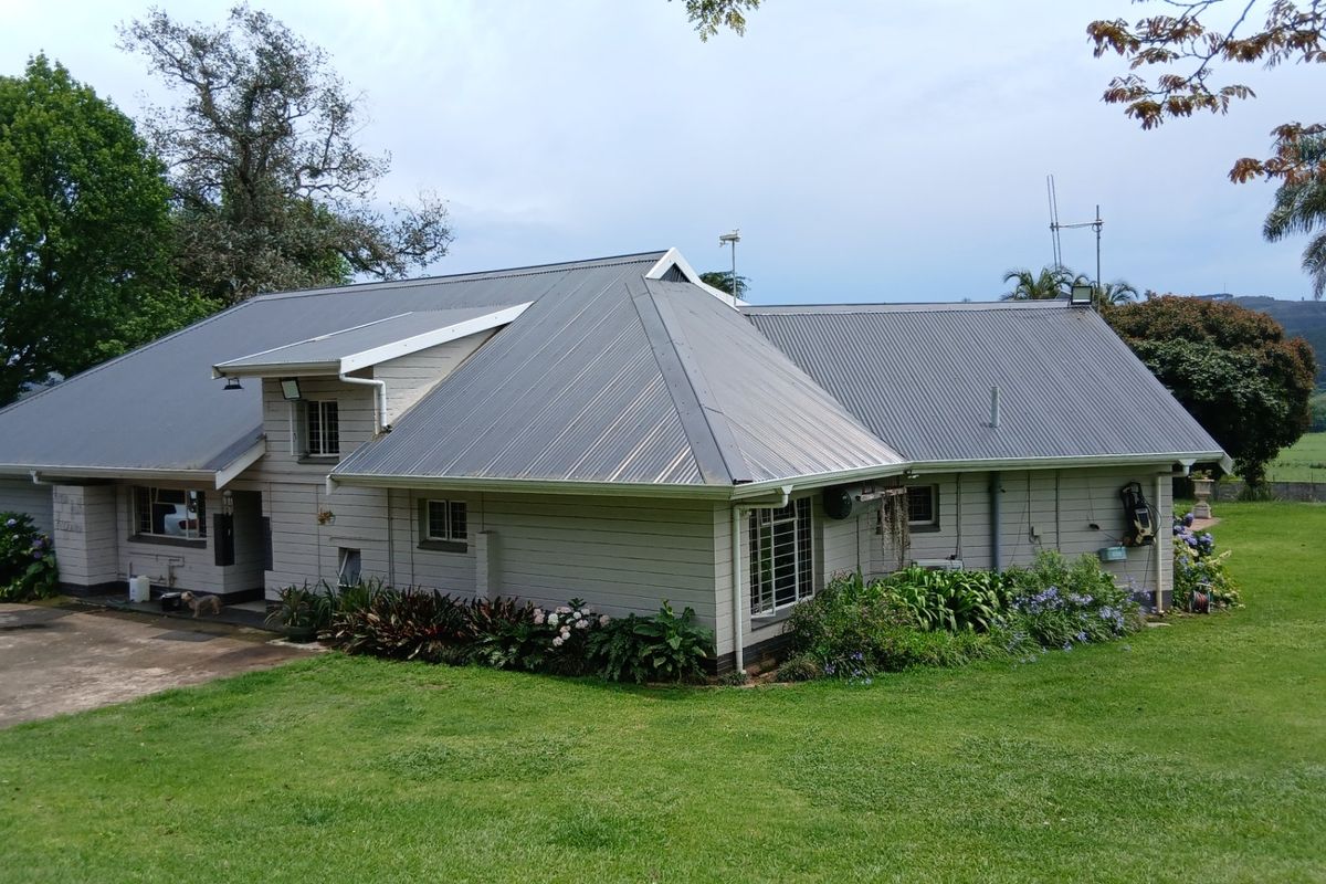Rear view of a farm-style residence featuring corrugated metal roofing, timber weatherboard cladding, and established garden surroundings on a spacious lawn.