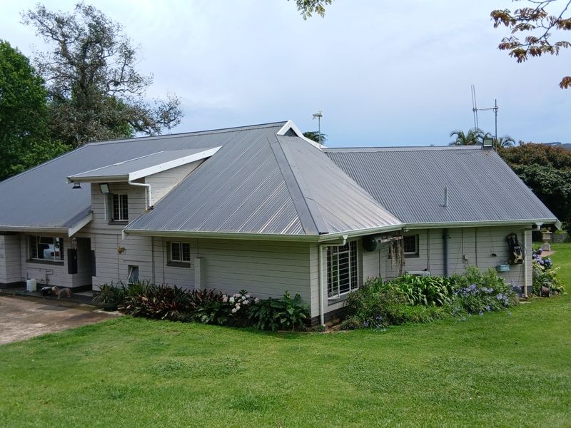 Rear view of a farm-style residence featuring corrugated metal roofing, timber weatherboard cladding, and established garden surroundings on a spacious lawn.