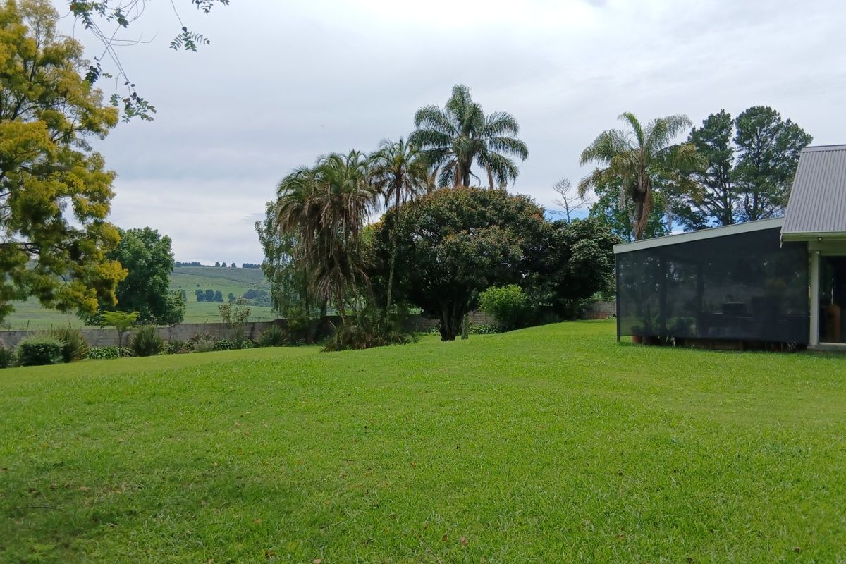 A spacious, well-maintained garden area featuring mature trees, expansive lawn, and a view of the surrounding rural landscape.