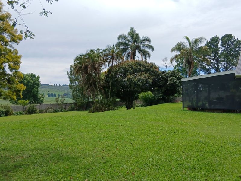 A spacious, well-maintained garden area featuring mature trees, expansive lawn, and a view of the surrounding rural landscape.