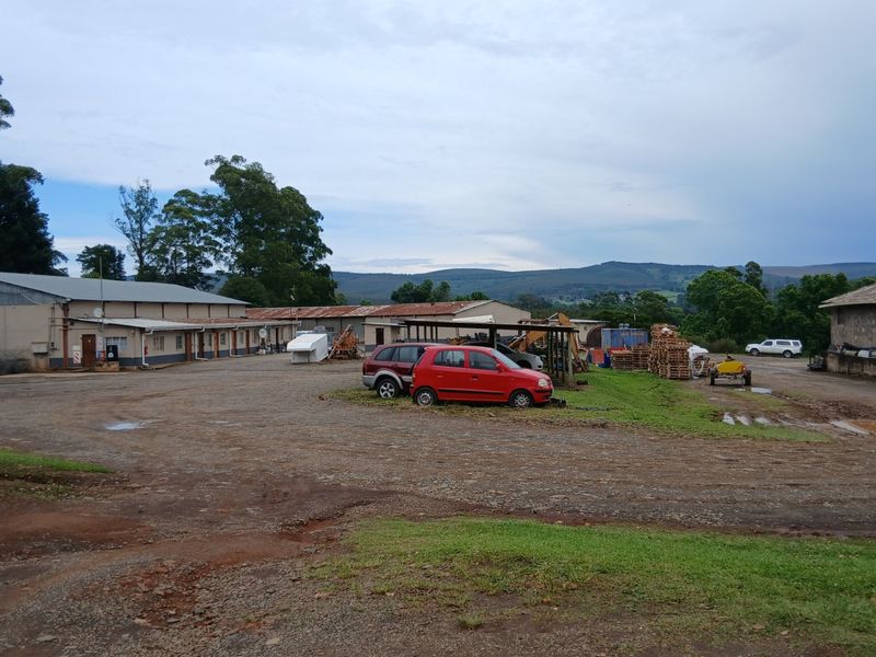 Wide view of the farm yard featuring multiple outbuildings with corrugated metal roofing and concrete block construction set against a rural landscape.