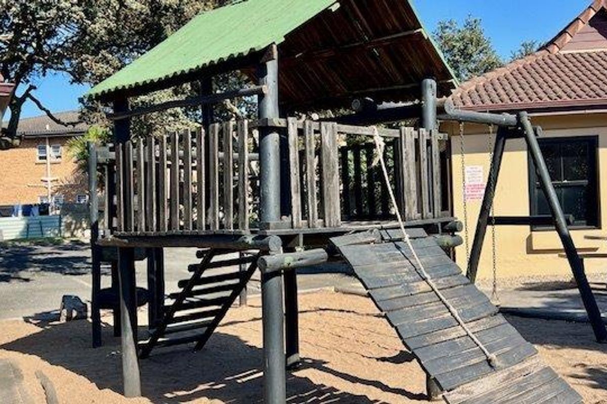 Outdoor communal area featuring a wooden jungle gym and swing set situated on a sand base within the apartment complex grounds.