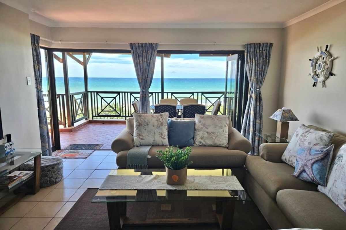 Spacious living room featuring tiled flooring and large sliding glass doors that open onto a balcony with expansive ocean views.