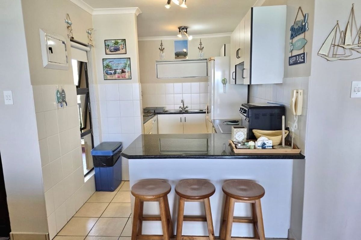 A functional kitchen featuring a granite-topped breakfast bar, tiled splashbacks, and ample built-in cabinetry, providing a practical and efficient cooking and dining space.