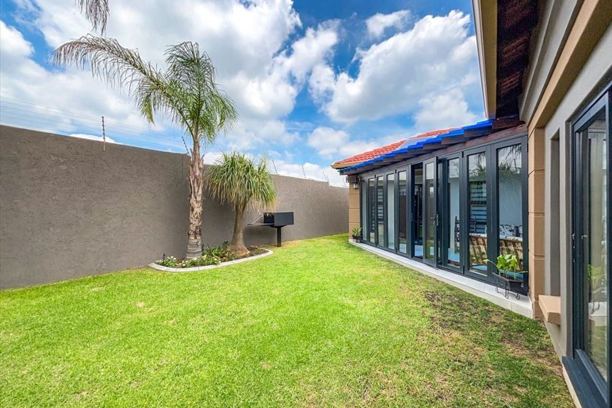 A well-maintained rear garden featuring a lawn, built-in braai, and modern folding glass doors providing seamless access to the interior living space.