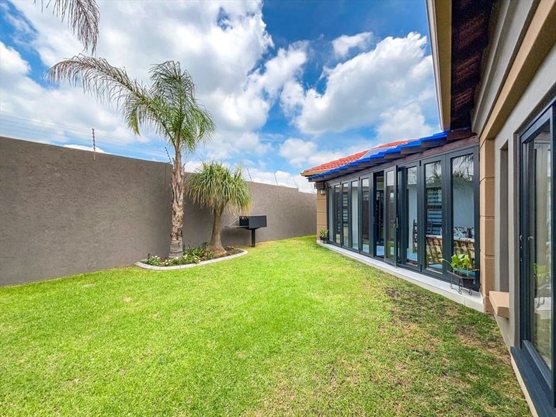 A well-maintained rear garden featuring a lawn, built-in braai, and modern folding glass doors providing seamless access to the interior living space.