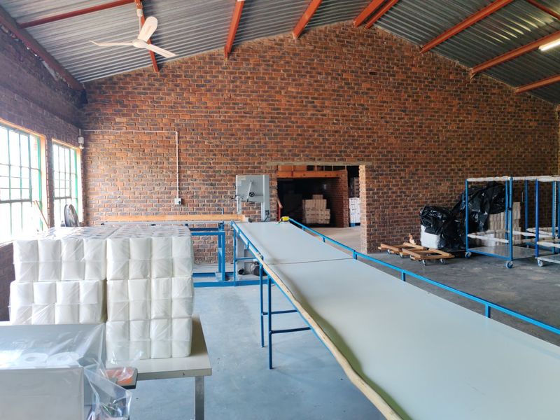 Spacious industrial utility area featuring exposed brick walls, high corrugated metal ceilings with steel trusses, and concrete flooring, suitable for storage or workshop use.