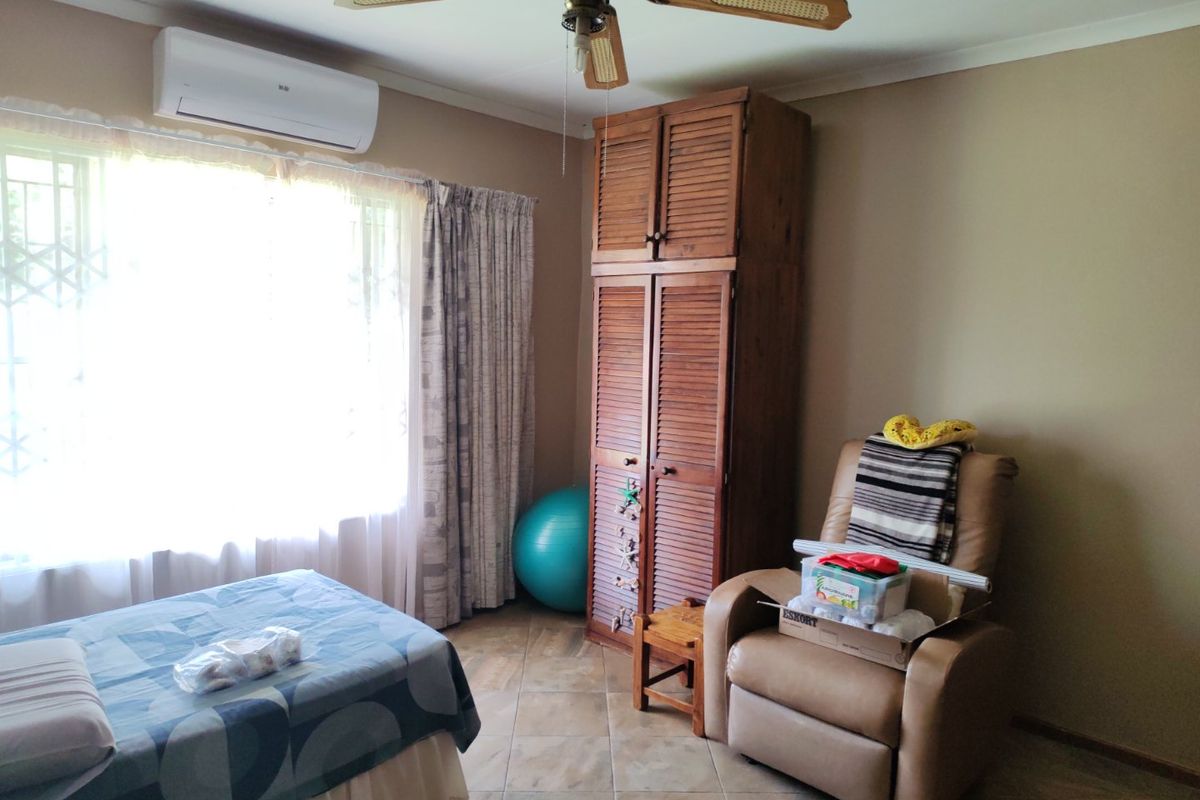 A bedroom featuring tiled flooring, a built-in wooden wardrobe, a ceiling fan, and a wall-mounted air conditioning unit.