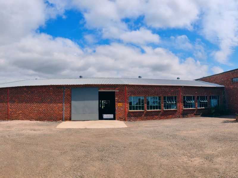 A wide-angle view of a large face brick farm building featuring a corrugated metal roof, industrial sliding door, and multiple steel-framed windows.