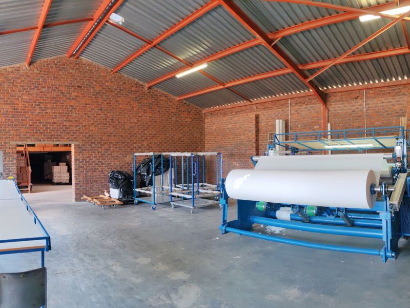 A spacious industrial utility area featuring exposed brick walls, high steel roof trusses, and durable concrete flooring, currently utilized for manufacturing or storage purposes.