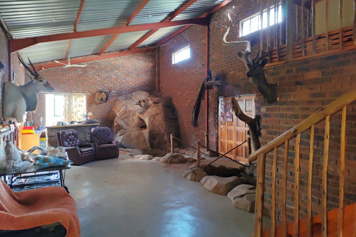 Spacious living area featuring exposed brick walls, steel roof trusses, a timber staircase leading to a mezzanine, and a unique built-in rock feature.