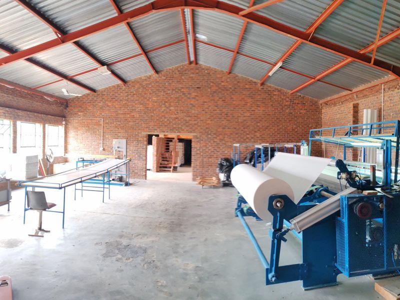 Spacious industrial utility shed featuring exposed brick walls, steel roof trusses, and concrete flooring, currently utilized as a manufacturing or storage workspace.