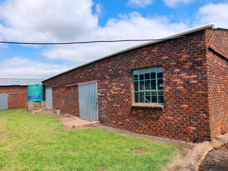 Rear view of a farm outbuilding featuring face brick construction, corrugated metal sliding doors, steel-framed windows, and an external water storage tank.