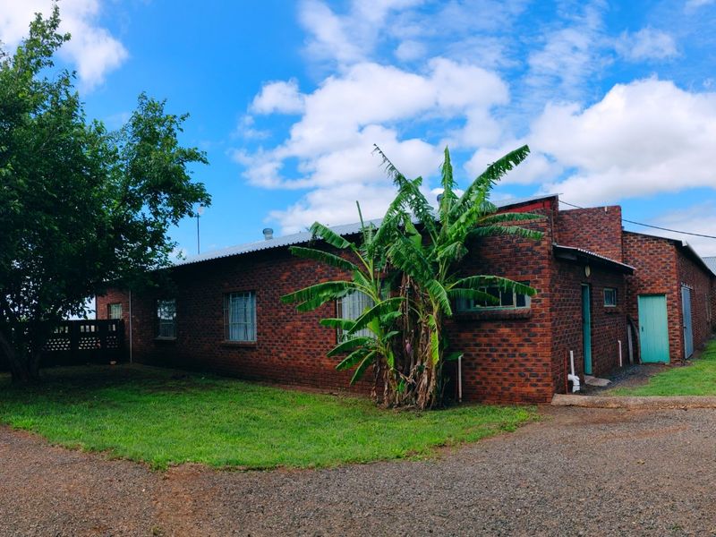 Rear view of a face brick farm building featuring a corrugated metal roof, security bars on windows, and an adjacent water storage tank.