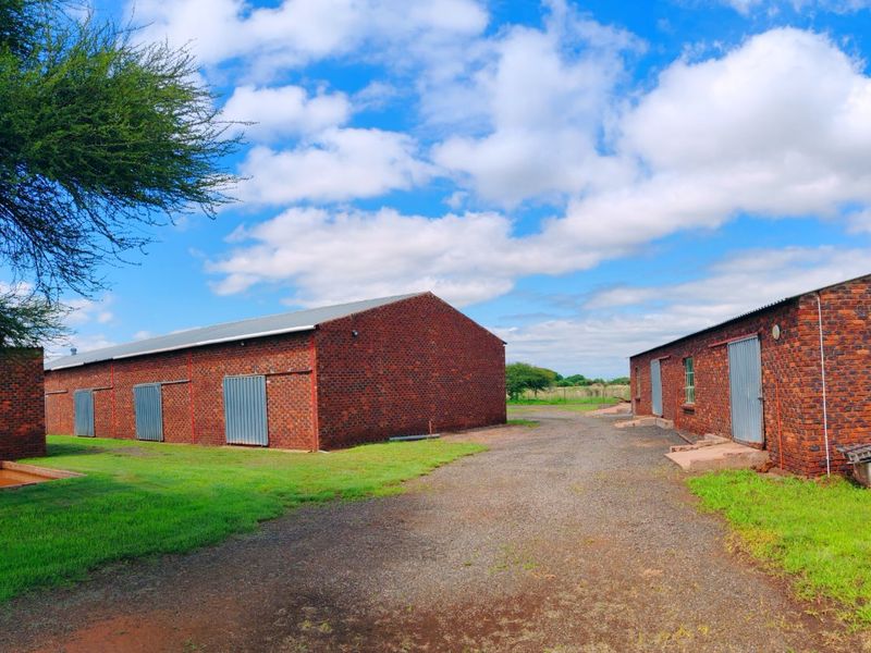 Exterior view of multiple brick farm outbuildings featuring metal roofing and steel-framed windows, situated on a gravel driveway with surrounding lawn.