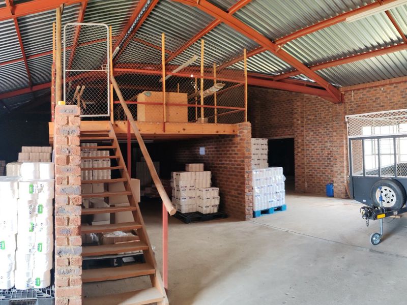 Spacious industrial utility shed featuring exposed brick walls, steel roof trusses, concrete flooring, and a functional mezzanine level with staircase access.