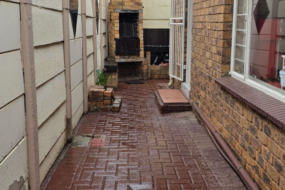 Rear exterior area featuring a brick braai, paved walkway, and secure boundary wall, offering a functional outdoor space for entertaining.
