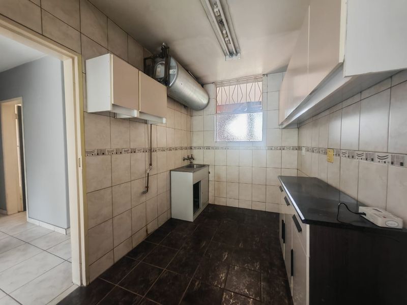 A functional kitchen space featuring tiled walls, built-in cabinetry, a sink, and an exposed electric water heater, ready for modernization.