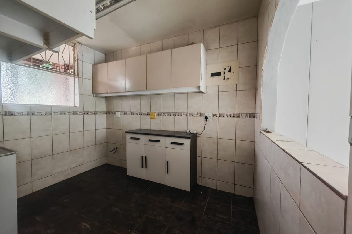A compact, empty kitchen featuring tiled walls and flooring, built-in cabinetry, and an exposed electrical distribution board requiring minor repairs.