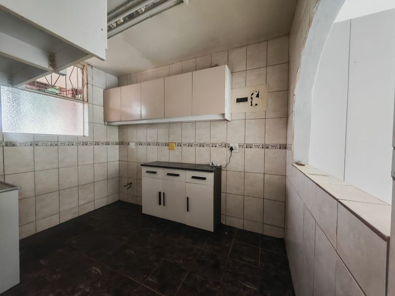 A compact, empty kitchen featuring tiled walls and flooring, built-in cabinetry, and an exposed electrical distribution board requiring minor repairs.