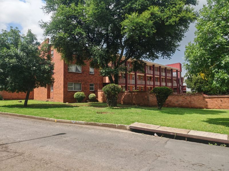 A view of the apartment building exterior featuring a red brick facade, balcony levels, and a well-maintained front lawn area.