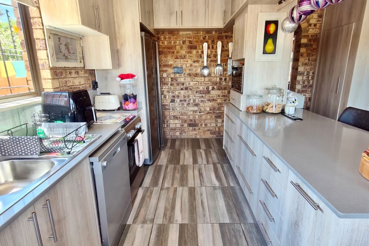 Modern kitchen featuring light wood-grain cabinetry, stone countertops, exposed brick feature wall, and integrated appliances with durable tiled flooring.