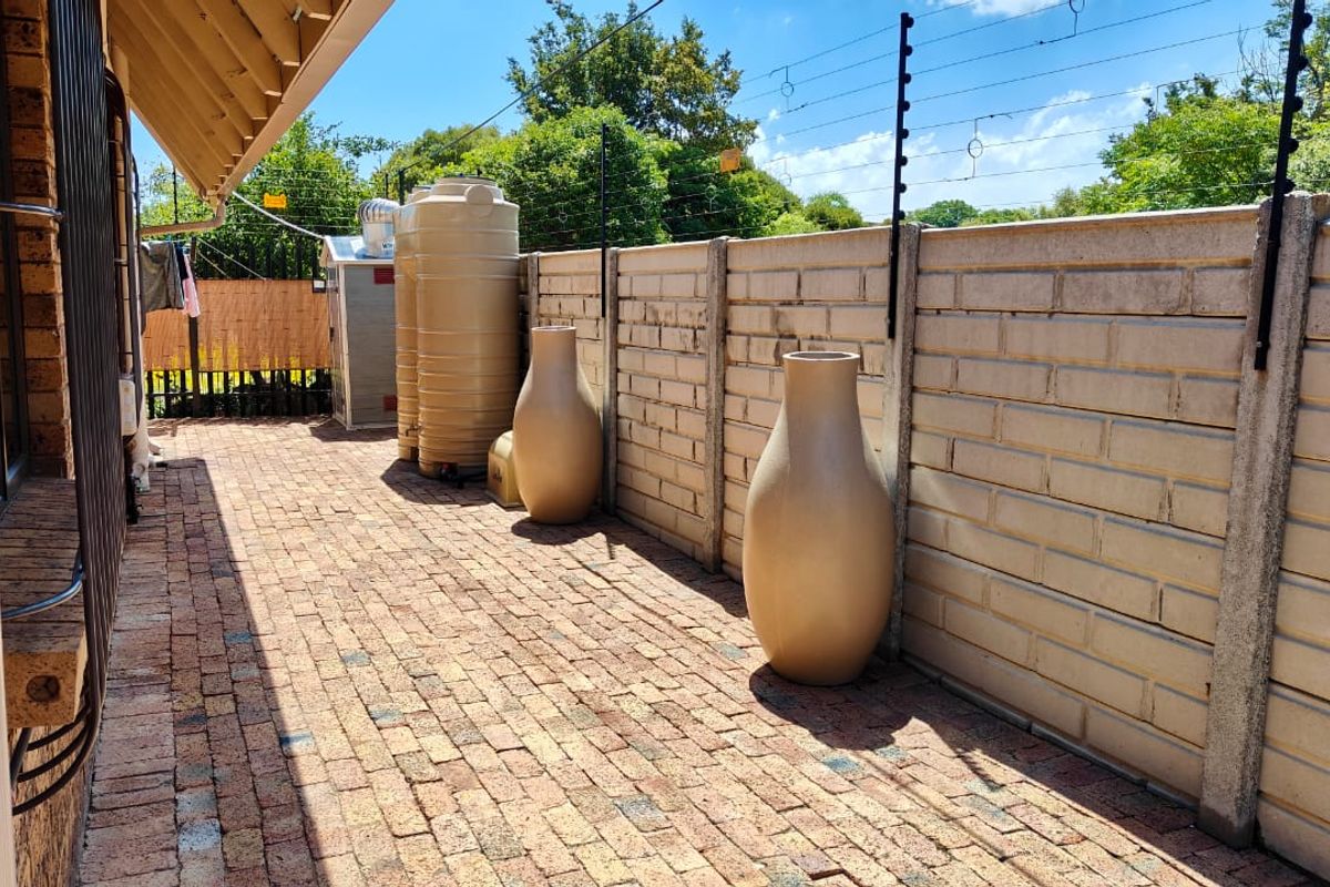 A paved rear exterior area featuring a precast concrete boundary wall with electric fencing and a water storage tank.