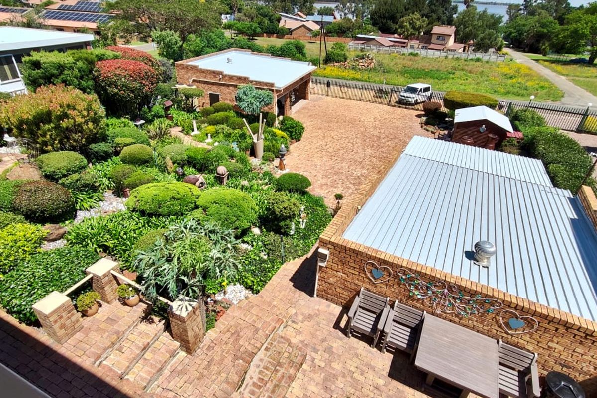Aerial view of a well-maintained property featuring a landscaped garden, brick-paved driveway, detached garage, and a spacious outdoor patio area.