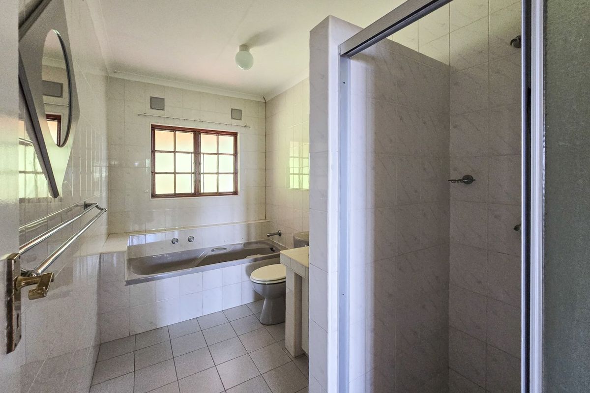 A functional bathroom featuring a built-in bathtub, separate shower enclosure, toilet, and vanity basin with tiled finishes throughout.