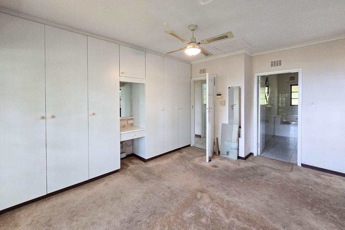 Spacious bedroom featuring extensive built-in cupboards, a vanity station, ceiling fan, and direct access to an en-suite bathroom.