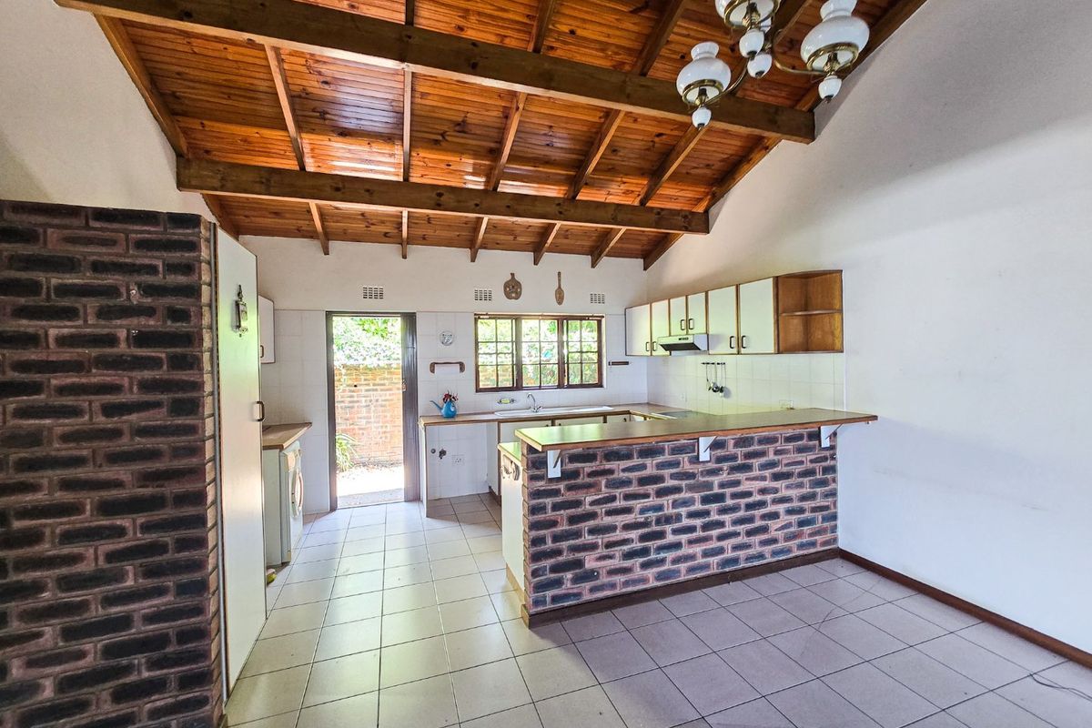 Spacious kitchen featuring a rustic exposed timber ceiling, brick breakfast bar, tiled flooring, and direct access to the rear exterior.