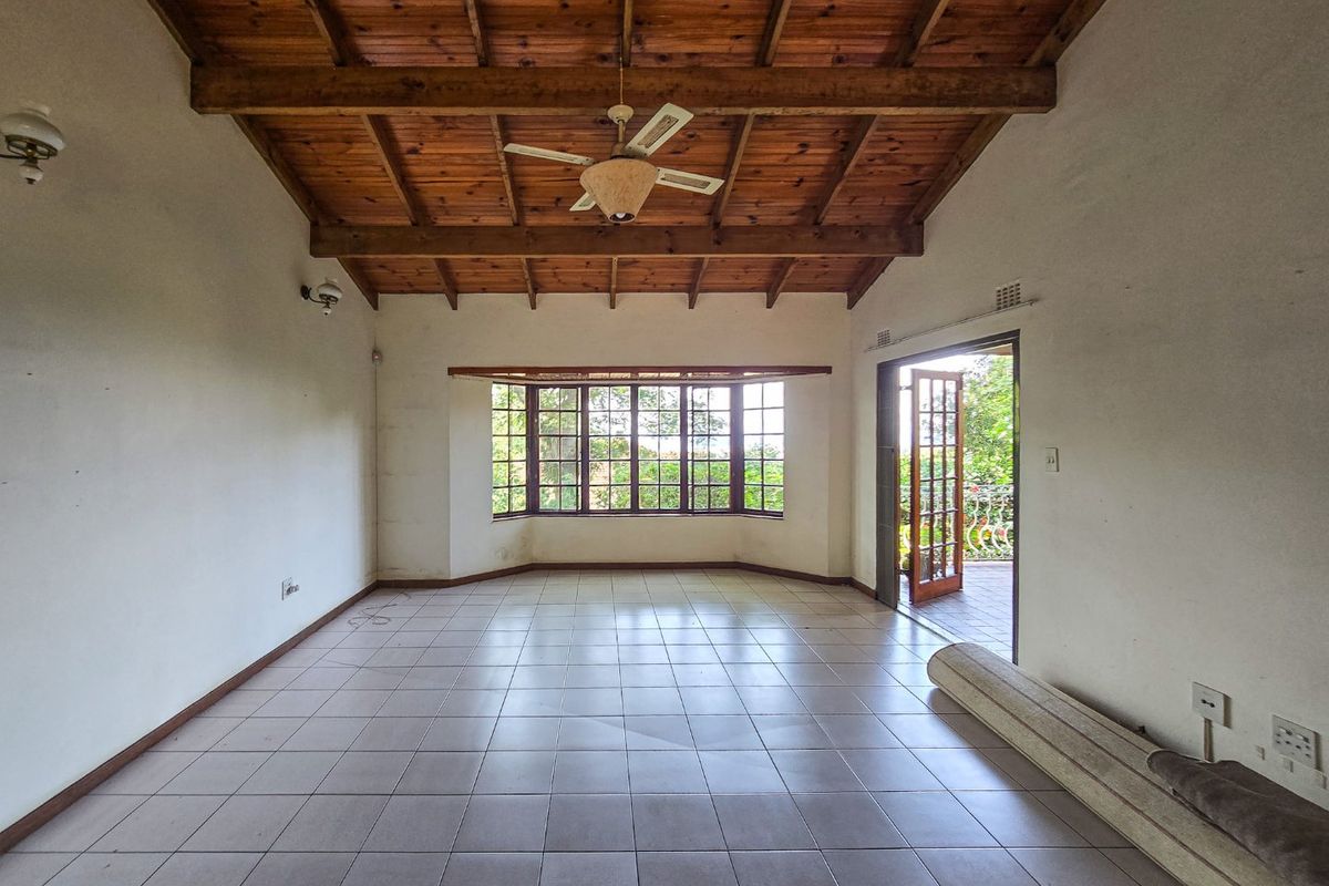 Spacious living room featuring an exposed timber beam ceiling, tiled flooring, and a large bay window with direct access to an outdoor patio area.