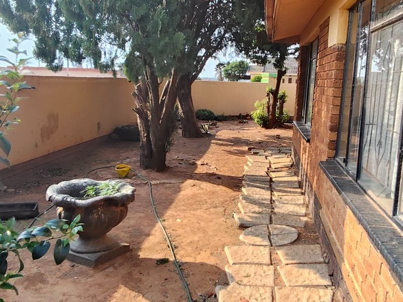 Rear exterior view featuring a brick facade, a stone pathway, and a perimeter boundary wall with mature trees in the garden area.