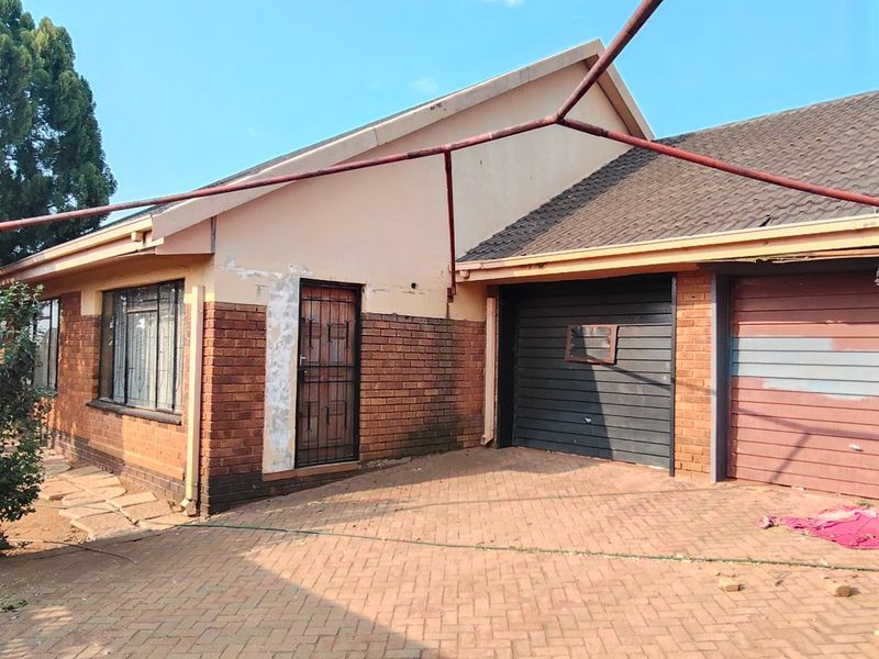 Front exterior view of a brick house featuring a double garage, paved driveway, and a metal carport structure.