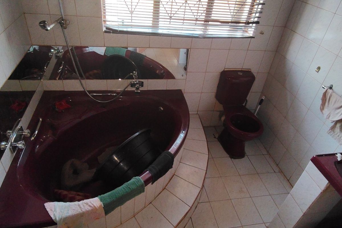 A dated bathroom featuring a corner bathtub, toilet, and vanity basin with full-height wall tiling and floor tiles.