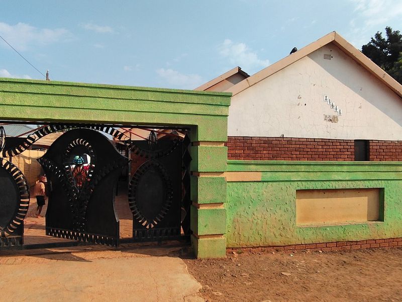 Front view of a residential property featuring a prominent green perimeter wall, metal security gate, and a brick and plaster facade.