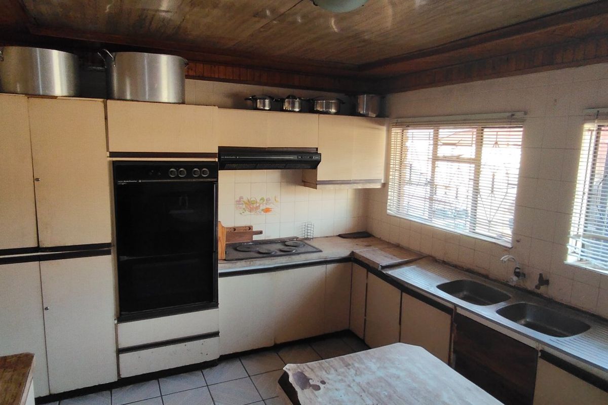 A dated kitchen featuring original cabinetry, integrated oven, electric hob, and double stainless steel sink with tiled flooring and a timber ceiling.