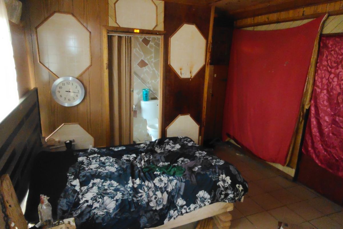 A bedroom featuring wood-paneled walls and tiled flooring, requiring significant cosmetic updates and repairs to improve the overall condition and aesthetic appeal.